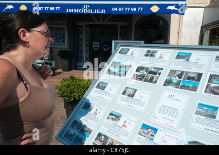 Une femme regarde les détails des villas de vacances à vendre ou à louer à l'extérieur d'un des agents immobiliers à Marseillan, dans le sud de la France. Banque D'Images