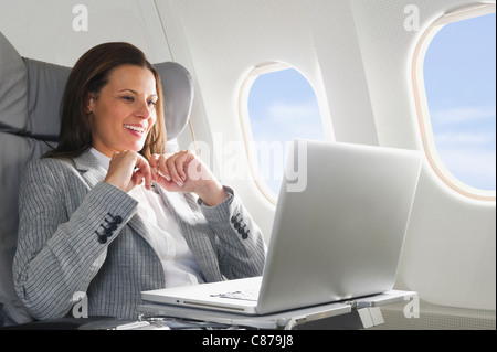 Germany, Bavaria, Munich, Mid adult businesswoman using laptop in airplane cabin Banque D'Images