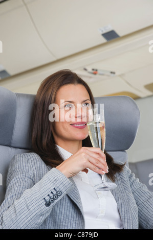 Germany, Bavaria, Munich, Mid adult woman drinking champagne in airplane cabin Banque D'Images