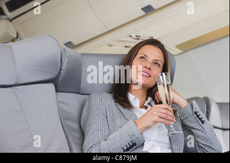 Germany, Bavaria, Munich, Mid adult woman drinking champagne in airplane cabin Banque D'Images