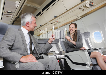 Germany, Bavaria, Munich, Businessman and woman toasting with champagne in airplane cabin, smiling Banque D'Images