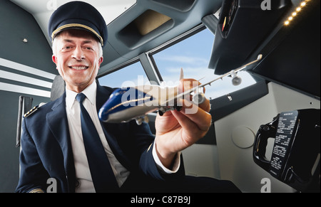 Germany, Bavaria, Munich, Senior pilot holding model airplane in airplane cockpit Banque D'Images