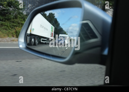 Une voiture tractant une caravane vers le bas l'autoroute reflète dans une voiture wing mirror Banque D'Images