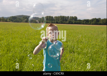 L'Allemagne, en Rhénanie du Nord-Westphalie, Hennef, Boy blowing bubbles de bubble wand in meadow Banque D'Images