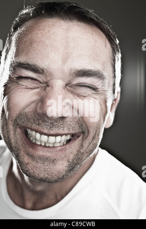 Close up of mature man making funny faces sur fond noir, smiling Banque D'Images