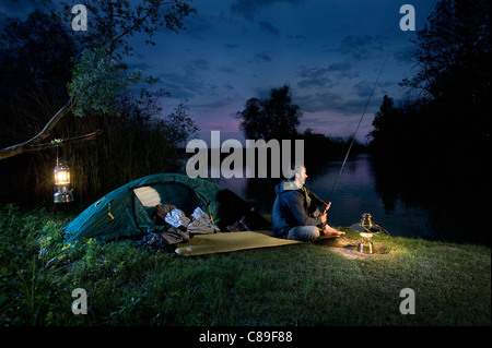 Allemagne, Bavière, Ammersee, homme assis près de lac avec lanterne et de pêche au crépuscule Banque D'Images