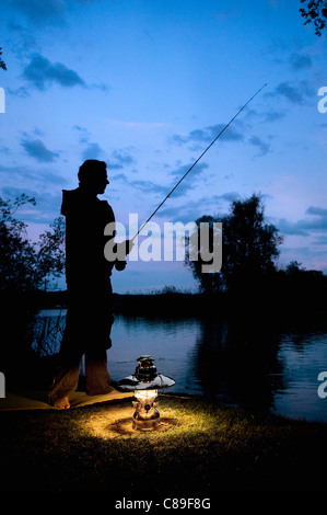 Allemagne, Bavière, Ammersee, homme assis près de lac avec lanterne et de pêche au crépuscule Banque D'Images