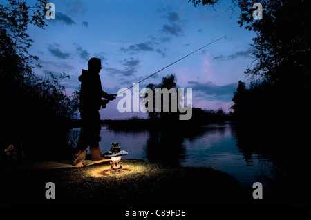 Allemagne, Bavière, Ammersee, homme assis près de lac avec lanterne et de pêche au crépuscule Banque D'Images