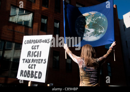 Une femme nous tend un drapeau avec une image de la terre sur elle , à côté d'un panneau disant 'Entreprises devenir riche, les contribuables voler Banque D'Images