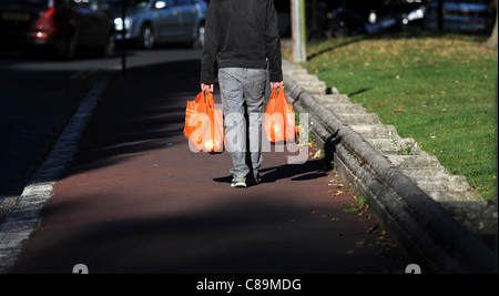 Homme marchant le long de la rue de la chaussée ou avec des sacs en plastique de supermarché Sainsburys UK Banque D'Images