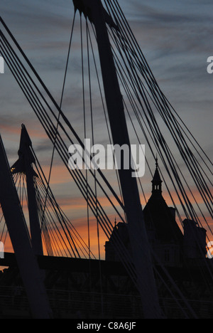 Londres coucher du soleil vu de la rive sud de la Tamise à travers des supports de Hungerford Bridge un soir d'été. Banque D'Images