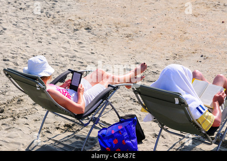 Femme lit de son Kindle et homme son livre à West Wittering pendant le week-end exceptionnellement chaud du 1er octobre 2011, West Sussex, Angleterre, Royaume-Uni Banque D'Images