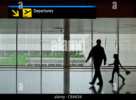 DÉPARTS DE L'AÉROPORT FAMILLE Père et jeune fille de 4-6 ans en silhouette sur le Concourse contemporain marcher à pied à la porte des départs du terminal de l'aéroport Banque D'Images