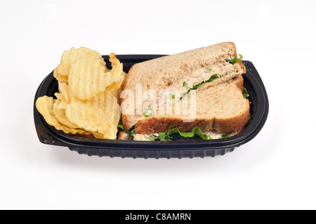 Sandwich au thon mayo avec céleri et laitue sur du pain complet coupé en deux avec des chips ou croustilles de pommes de terre dans un bac en plastique noir à emporter sur blanc, découpe. Banque D'Images