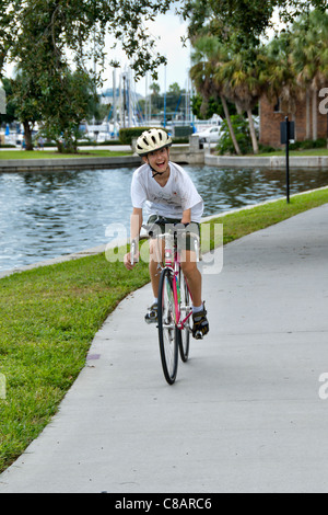 Un jeune homme sourit et monte un vélo le long d'une marina à Saint-Pétersbourg, en Floride. Banque D'Images