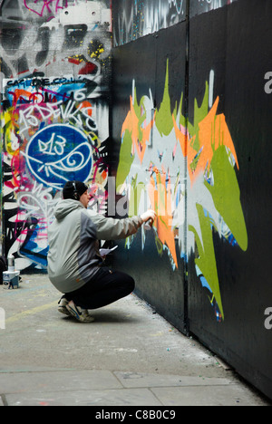 Graffiti artiste au travail sur South Bank, Londres portant une paire d'écouteurs Banque D'Images