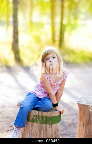 Kid girl blonde au tronc de l'arbre à l'extérieur de la forêt Banque D'Images