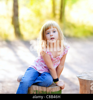 Kid girl blonde au tronc de l'arbre à l'extérieur de la forêt Banque D'Images