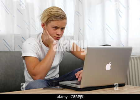 Adolescent en utilisant son Apple MacBook Pro pour faire leurs devoirs tout en gardant ses amis à jour sur les services de réseaux sociaux Banque D'Images