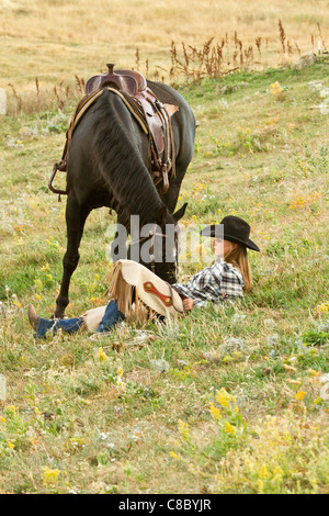 Cowgirl reposant parmi les fleurs sauvages dans un champ à côté de son cheval Banque D'Images