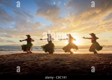 Quatre danseurs hula au coucher du soleil à Palauea, Maui, Hawaii, éclairé par le soleil. Banque D'Images