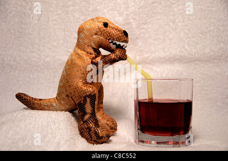 Un dinosaure T Rex en peluche, assis, tenant une paille bendy, buvant du jus de cassis à partir d'un verre. Banque D'Images