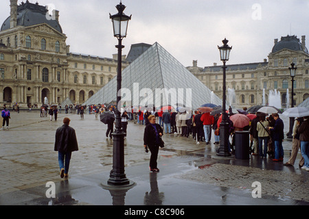 Paris. La France. Une longue file d'attente de touristes dans la pluie d'entrer dans le musée du Louvre. 1e arrondissement. Banque D'Images