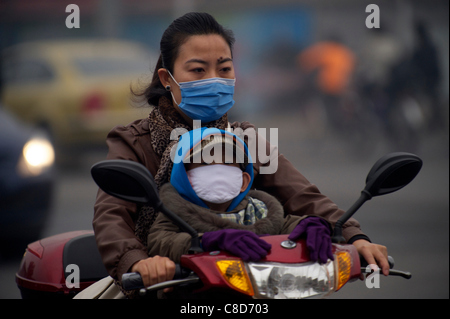 Une mère et son fils portent des masques sur le chemin de l'école par un vélo à assistance électrique dans un air pollué matin à Beijing, Chine le 20 octobre 2011. Banque D'Images