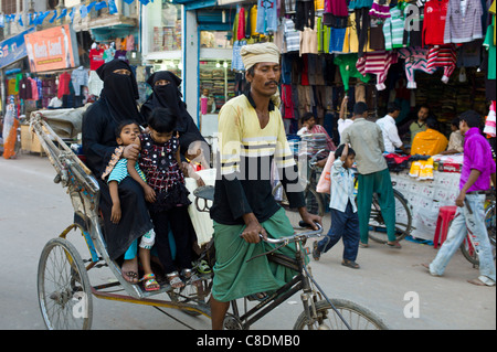 Scène de rue dans la ville sainte de Varanasi, les jeunes femmes musulmanes en burkhas noir ride avec leurs enfants en rickshaw, Inde Banque D'Images