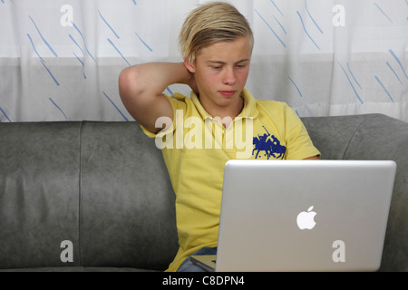 Adolescent en utilisant son Apple MacBook Pro pour faire leurs devoirs tout en gardant ses amis à jour sur les réseaux sociaux Banque D'Images