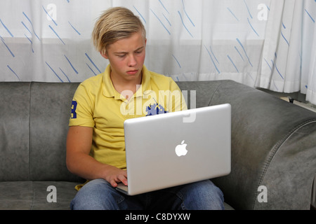 Adolescent en utilisant son Apple MacBook Pro pour faire leurs devoirs tout en gardant ses amis à jour sur les réseaux sociaux Banque D'Images