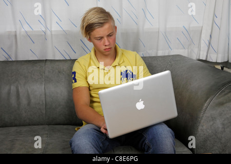 Adolescent en utilisant son Apple MacBook Pro pour faire leurs devoirs tout en gardant ses amis à jour sur les réseaux sociaux Banque D'Images