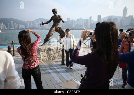 Des touristes posent pour des photos en statue de Hong Kong arts martiaux et star du film Bruce Lee (1940-73) sur l'Avenue des Stars. Banque D'Images