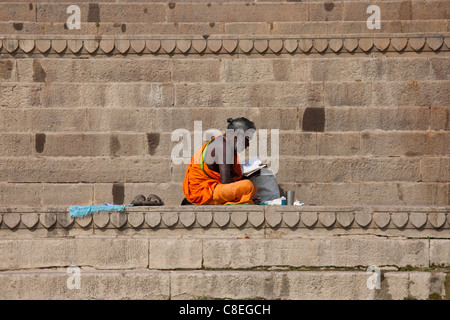 Sadhu hindou avec saint homme robe traditionnelle se lit sur les marches des Ghats dans la ville sainte de Varanasi, Benares, Inde du Nord Banque D'Images