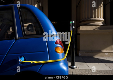 Un câble d'alimentation se branche sur la place d'un bouchon d'essence pendant le rechargement de G-Wiz voiture dans le centre de Londres. Banque D'Images