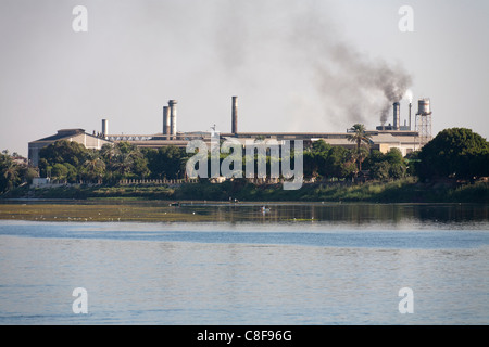 Une section de Nil bank des complexes industriels avec cheminées fumer derrière la banque d'arbres et plusieurs petits bateaux de pêche Banque D'Images