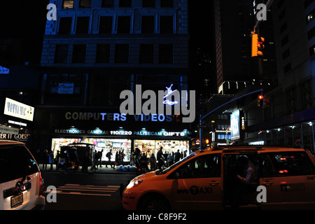 Vue de nuit en taxi jaune garé, personnes à pied bleu avant la vidéo informatique magasin de l'autre côté de la route, 7e Avenue Ouest 50e Rue, New York Banque D'Images