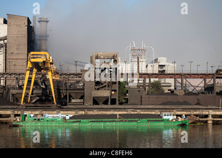 Une section de Nil bank des complexes industriels crachent de la fumée et le charbon péniche amarrée au quai en face reflète dans l'eau Banque D'Images