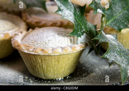 Close up of mince pies saupoudrés de sucre glace sur la plaque noire avec des branches de houx Banque D'Images