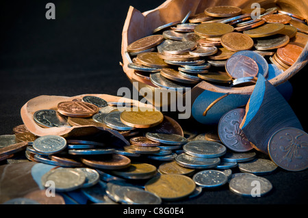 Broken terramundi pot d'épargne avec de l'argent s'échappe au-dessus de la table sur un fond noir Banque D'Images