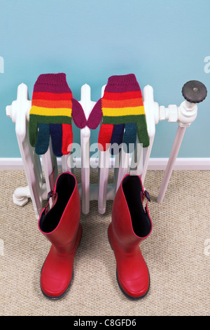 Photo de gants stripey et rouge séchage wellies sur un vieux radiateur en fonte traditionnelle dans un couloir, Banque D'Images