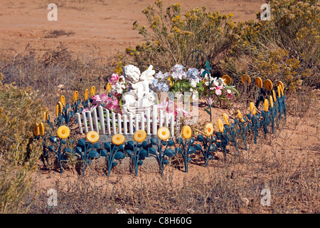 Cimetière négligé, envahie par les mauvaises herbes avec angel, fleurs en plastique,clôture blanche et des roches et des pierres autour de monticule de terre. Banque D'Images