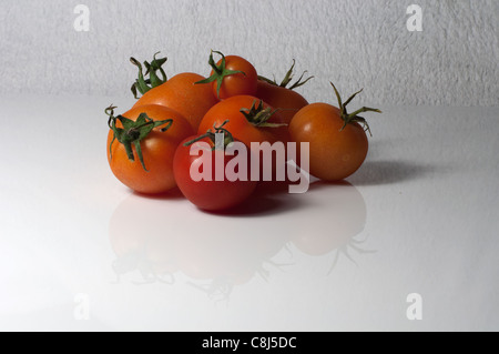 Homegrown tomatoes assis sur un ensemble de perspex blanc contre un fond blanc. Les tomates reflétant dans le livre blanc.. feuille de plexiglas Banque D'Images