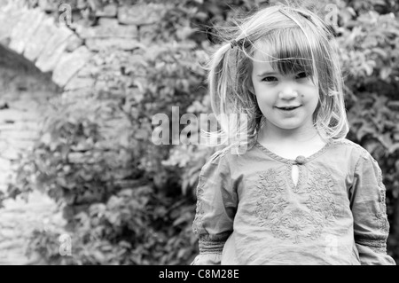 Portrait noir et blanc d'une petite fille debout à l'extérieur dans un jardin Banque D'Images