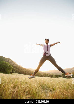 Mixed Race woman jumping in remote field Banque D'Images