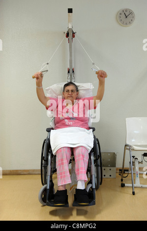 Femme en fauteuil roulant de faire des exercices de réadaptation physique au gymnase de physiothérapie de l'hôpital. Banque D'Images