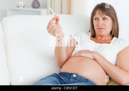 Belle femme enceinte tenant une cigarette tout en se trouvant sur un canapé Banque D'Images