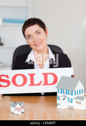 Portrait d'un agent immobilier avec un panneau vendu et maisons miniatures Banque D'Images