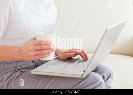 Close up of a woman holding a cup ayant un ordinateur portable sur ses genoux Banque D'Images