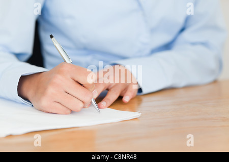 Vue frontale d'une jeune femme écrit sur une feuille de papier en position assise Banque D'Images